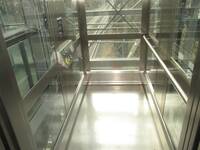 Ein gläserner Aufzug mit einem Metallboden und Tastatur und Handlauf