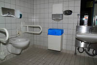 Behindertentoilette weiß gefliest, links Toilette mit Haltegriffen, rechts Waschbecken
