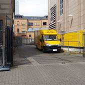 Einfahrt links von Postgebäude, rechts Packstation und DHL-Fahrzeug