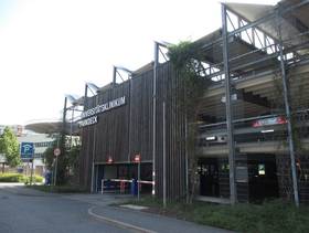 Gebäude mit 3 Ebenen, die Aussenseite ist zum Teil mit Holz verkleidet und mit Metallstreben versehen, links im Gebäude ist die Parkhauseinfahrt, über der Einfahrt der Name des Parkhaus
