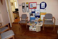 gepolsterte Holzstühle, dazwischen Beistelltisch mit Broschüren, links  davon Zugang zu Beratungsbüro