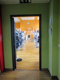 offene einflügelige Tür, dahinter einige Fitnessgeräte auf einem Parkettboden