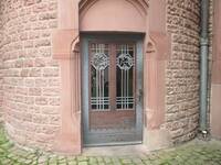 Alte zweiflüglige Holztür mit Glaseinsätzen und schmiedeeisernen Elementen vor den Scheiben.  Die Tür befindet sich in einem turmähnlichen Rundbau