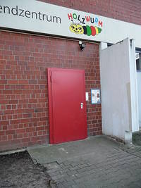 eiflüglige rote Tür, davor unebener geplasteter Boden aus Betonverbundsteinen