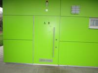 grüne Tür in einer grünen Wand, auf der Tür Symbol für Rollstuhlfahrere und Wickelkind, 