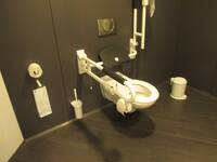 Eine weiße Toilette mit Haltegriffe rechts und links an einer schwarzen Wand