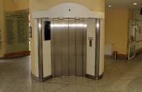 metalische Fahrstuhltür mit weißer Umrandung,davor Bodenbelag aus Fliesen