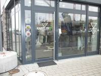 Ladenfront aus Glas, an der Ecke Eingangstür mit senkrechter Griffstange, davor liegt ein Schmutzabweiser