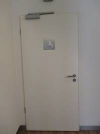 Weiße Tür vor weißer Wand, auf der Tür ein Rollstuhlfahrersymbol