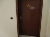 Eine hölzene Tür in einer weißen Wand mit einem Rollstuhlfahrer Symbol 