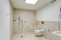 hell gekachelter Raum mit Dusche, Behindertentoilette und Waschbecken