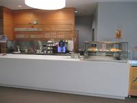 Servicetheke mit Glaskasten mit Kuchen auf der linken Seite, trennt den Gastraum von der Küche ab, hinter der Theke Regal mit Gläsern und Kaffeemaschiene  