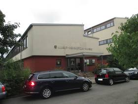zwei beieinander stehende Gebäude, auf dem linken Gebäude Schriftzug "Albert Schweitzer Schule" und ein überdachter Eingang mit Stufen, davor Straße mit parkenden Autos