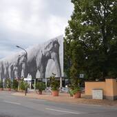Langes, rechteckiges Gebäude, Gebäudeseite zur Straße hin mit Längslamellen mit Elefantenmotiven. Der Eingang zu den Zookassen und Zooshop befindet sich im rechten Gebäudeteil, das Parkhaus im linken.