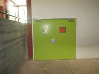 zweiflügelige grüne Tür in einer hellen Wand, links eine Mauer bis zum Erdgeschoss