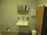 Weißes Waschbecken an einer hellen Wand. Über dem Waschbecken ist ein Spiegel und auf beiden Seiten ist ein Seifen- bzw. Desinfektionsmittelspender