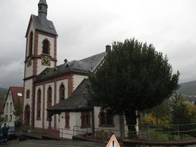 Kirche mit einem Kirchturm. Davor ein Baum