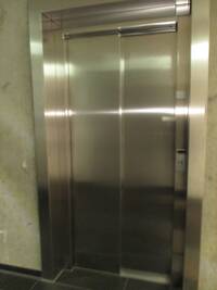 Edelstahl-Aufzug mit geschlossener Tür in einer unverputzten Betonwand