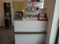 weiße Theke mit verschiedenen Artikeln, dahinter ein Regal mit Produkten, links neben dem Regal Tür zu einem Behandlungsraum