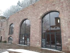 Sandsteinbau mit 3 großen Rundbogenfenster, im ersten rechts ist ein Eingang,