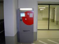 Parkautomat, links oben ist ein Bildschirm mit Tasten, unter dem Bildschirm ist ein Geldeingabschlitz und eine Parkticketannahme. Im oberen Bereich ist ein roter Kreis aufgemalt