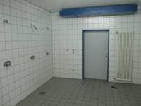 weiß gekachelter Raum mit drei Duschplätzen, an der vorderen Wand ist eine geschlossene Tür und daneben ein weißer Heizkörper