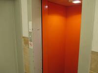 Organgefarbener Aufzug mit offenstehender Tür in einer weißen Wand