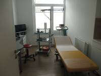 Ein Raum mit einer Liege, verschiedenen medizinischen Geräten und einem Tisch mit Computerbildschirm