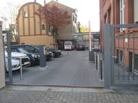 Eine Einfahrt mit hochgeklappter Schranke. Links ist der Parkplatz, rechts das Gebäude.