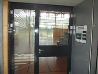Glaselement mit Tür, links Glasfläche. Dahinter Sporthalle mit breiter Glasfront