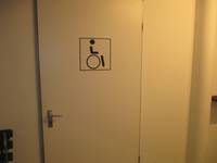 Eine weiße Tür in einer weißen Wand, auf der Tür ist eine Rollstuhlsymbol