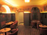 Gastraum mit hoher Wandverkleidung aus dunkelgrauem Holtz, darauf sind verschiedene Wappen aufgemalt. Darüber sind die Wände komplett mit mittelalterlich wirkenden Wandmalereien bedeckt. Tische und Polstersessel vorhanden.