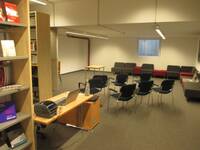 Ein großer Raum, an der linken Wand stehen Bücherregale. Großer Raum mit Stühlen darauf und Sesseln