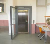 offener Aufzug mit einer offen Tür die vor dem Aufzug ist, links steht ein tisch