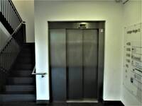 Eine geschlossene Aufzugtür aus Edelstahl, links daneben aufwärts führende Treppe