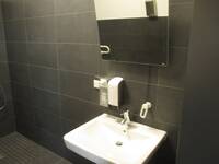 Ein weißes Waschbecken an einer schwarzen Wand mit einem Seifenspender und einem kippbaren Spiegel