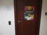 dunkelbraune Tür in weißer Wand. Auf der Tür ist ein großes buntes Plakat mit gelben Smileys und der Aufschrift: Queer Youth Heidelberg