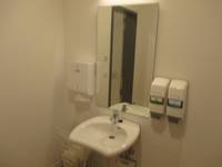 Waschbecken mit Spiegel, links Papierhandtuchhalter, rechts zwei Seifenspender 