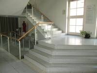 Eine nach oben verlaufende Treppe in einem Foyerbereich. Der untere Teil der Treppe ist Breiter und führt zu einem größeren Podest.