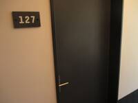 Dunkle Türe in einer hellen Wand, links daneben hängt ein Schild mit der Zimmernummer 127
