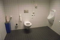 gekachelter Raum, Toilette gegenüber Eingang, Notrufseil neben rechtem Handgriff. Wachbecken und Pissoir auf rechter Seite