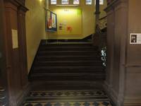Treppe mit Podest und Handlauf rechts, gefliestes Muster vor der Treppe, auf dem Podest bewegliche Pinwand 