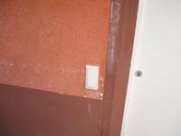 weißer Taster an einer roten Wand, rechts daneben ein Stück einer weißen Tür
