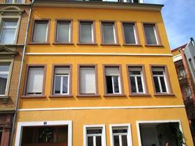 dreistöckiges gelbes Gebäude, auf der Fassade sieht man Fenster mit roten Rahmen