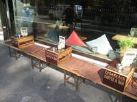 Vor einem Schaufenster stehen Bänke mit Sitzkissen und umgedrehten Weinkisten als Abstellfläche für Geschirr