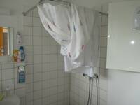 Ein gekachelte, leicht erhöhte Duschecke mit weißem Duschvorhang