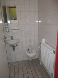 Toilettenraum mit Toilette und Waschbecken, links an der Wand eine Heizung