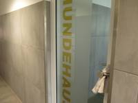  Glastür  mit senkrechten Schriftzug: Hundehaus. Um den  Griff ist ein Handtuch geschlungen, um das Zufallen der Tür zu verhindern. Rechts und links sind graue Wände