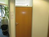Holztür, links davon Türschilder und ein offenstehendes Büro
