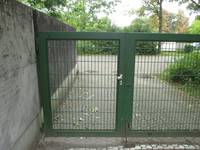 grün gestrichenes Gittertor, links eine Mauer, geradeaus ein Weg
